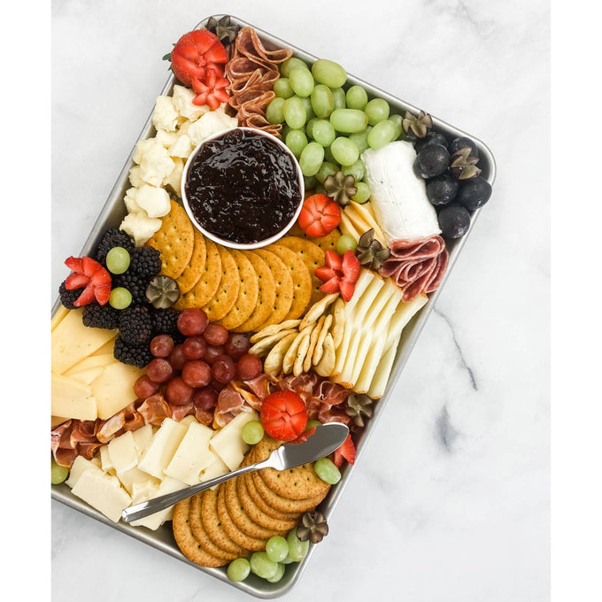 Aluminized steel baking pan filled with an arranged assortment of crackers, cheeses, sliced meats, grapes, blackberries, and a small bowl of dark fruit jam, featured in Kitchen & Food and USA Made collections.