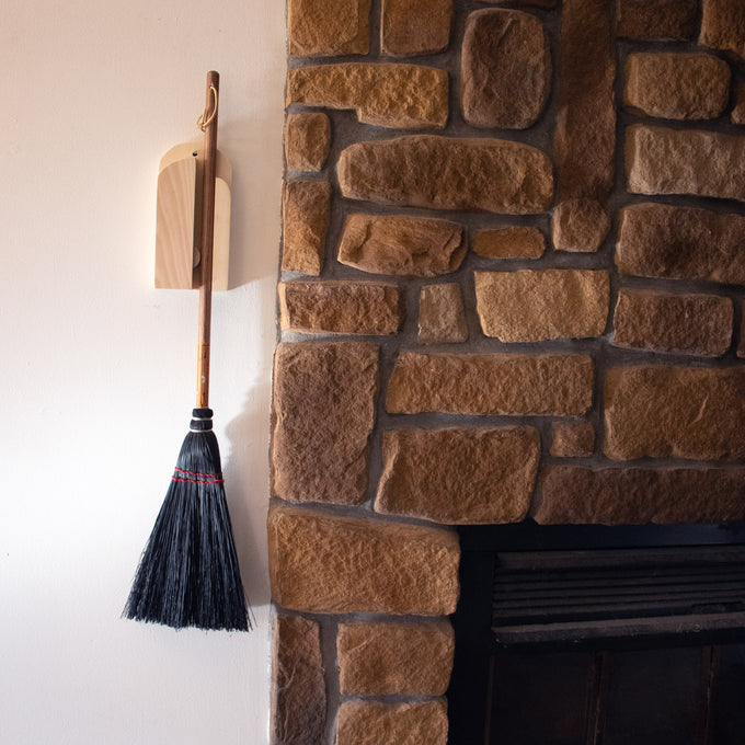 Handcrafted Amish made wooden wall-mounted broom holder securely storing a traditional broom next to a rustic stone fireplace, featured in Home & Decor and Household Helpers collections.