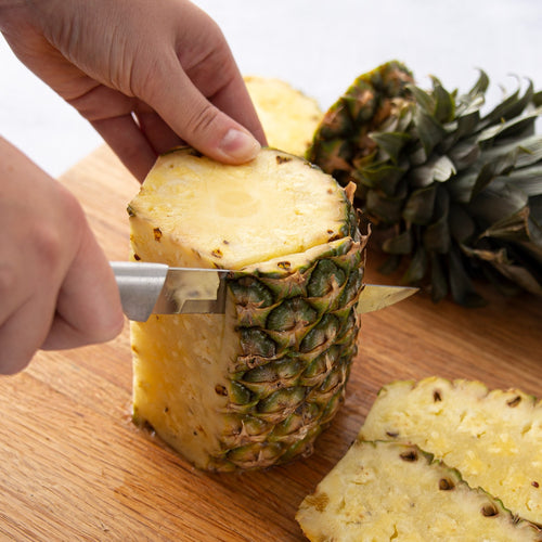 Handcrafted Rada Stubby Butcher Knife slicing a fresh pineapple on a wooden cutting board, featuring a stainless steel blade and silver brushed aluminum handle, ideal for Kitchen Knives and Food Prep collections.