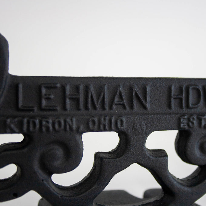 Close-up of a glossy black cast aluminum boot scraper featuring vintage scrollwork and embossed lettering, handcrafted in the USA, ideal for Home & Decor and Amish Made collections.