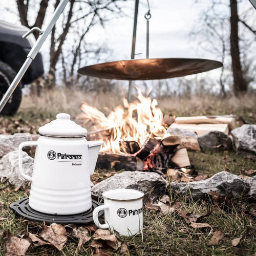 White enameled steel percolator and matching mug set placed on a cast iron trivet near a campfire with hanging cooking plate, ideal for camping and outdoor brewing, featured in Farm, Garden & Tool, Kitchen & Food, Camping, Brewing Coffee and Tea, Best Sellers, and Promo Eligible collections.