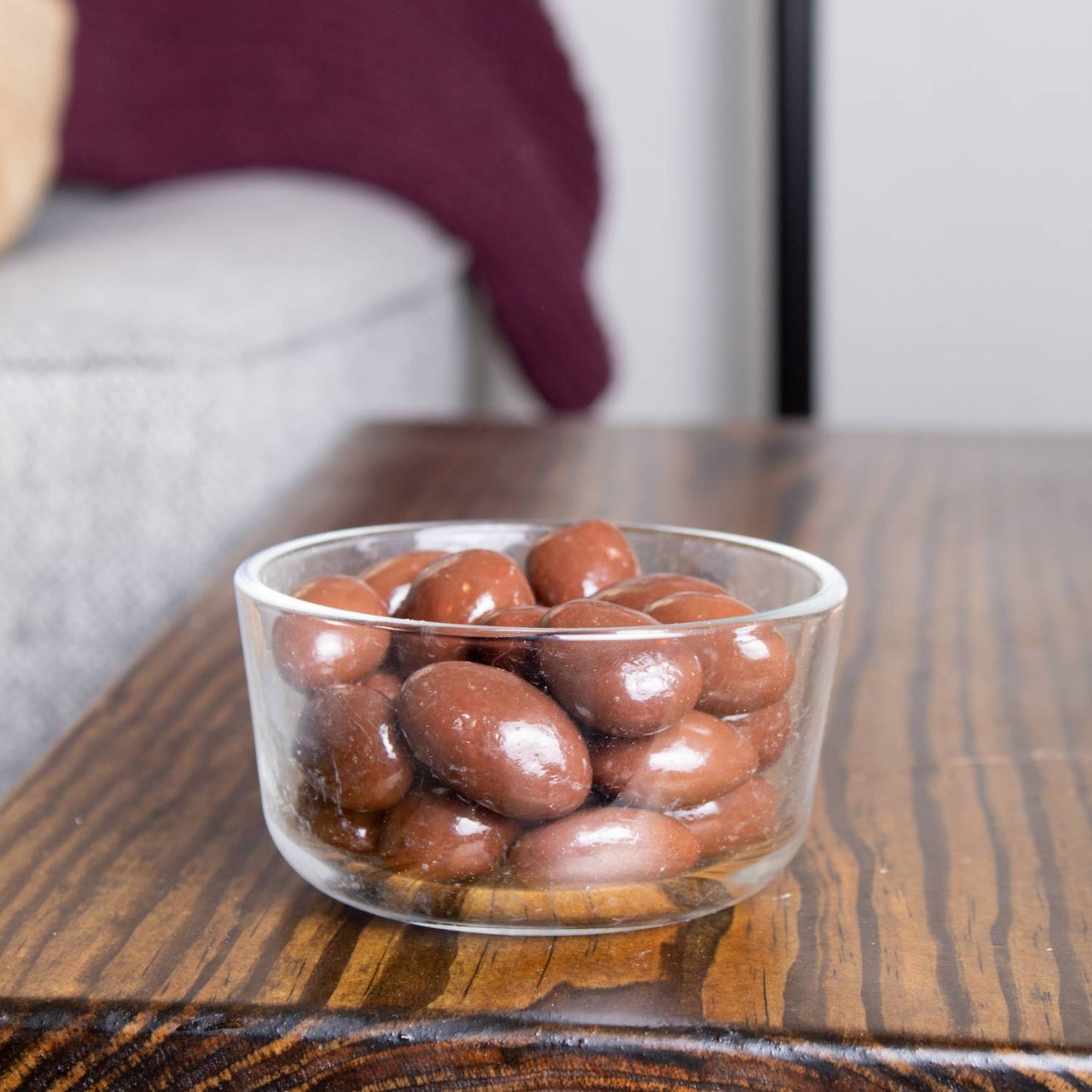 Clear glass bowl filled with glossy chocolate-covered almonds on a wooden table, featured in Kitchen & Food, Snacks and Sweets, Candy, USA Made, Best Sellers, and Promo Eligible collections.