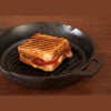 Handcrafted cast iron grill pan with raised ridges and assist handle, showing a grilled sandwich with melted cheese and tomato, ideal for Kitchen & Food, Cookware, Cast Iron, USA Made, Best Sellers, Promo Eligible collections.