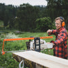 Person wearing protective earmuffs and goggles operating an orange bar nose steering accessory on a chainsawmill to align the guide bar for precise wood cutting in a green outdoor setting, featured in Farm, Garden & Tool and Wood Cutting and Hauling collections.