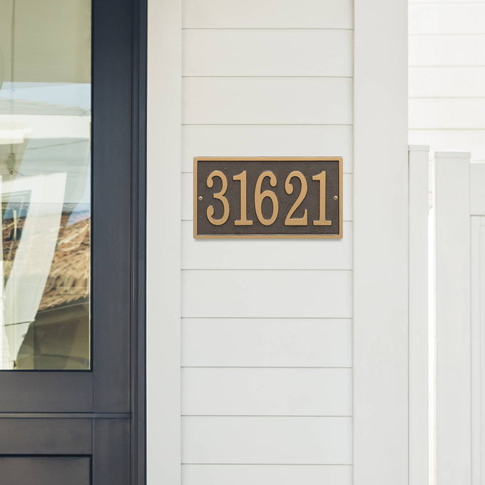 Bronze and gold rectangular custom address plaque mounted on white siding next to a black-framed glass door, handcrafted in USA, suitable for Home & Decor and Mailboxes and Address Signs collections.