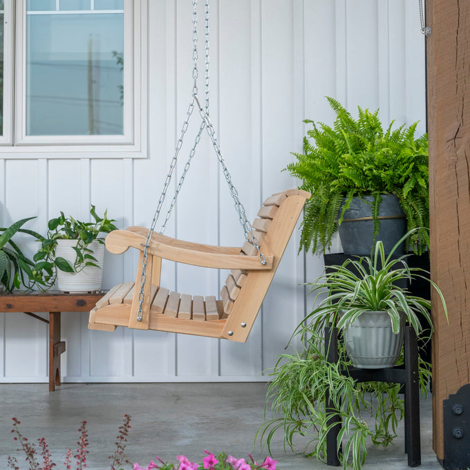 Handcrafted Amish made cypress swing with smooth slats and curved armrests, suspended by sturdy metal chains on a porch decorated with green plants, perfect for outdoor furniture collections.