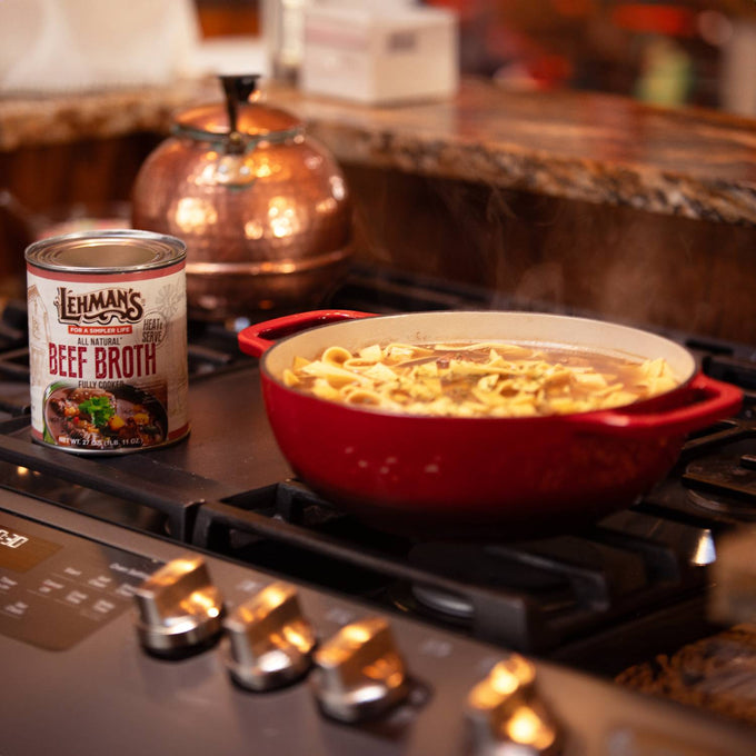 Can of handcrafted beef broth next to a red enamel pot simmering noodles on a stovetop in a warm kitchen setting, perfect for Farm, Garden & Tool, Kitchen & Food, Emergency Supplies, Food, Meats, Best Sellers, and Promo Eligible collections.