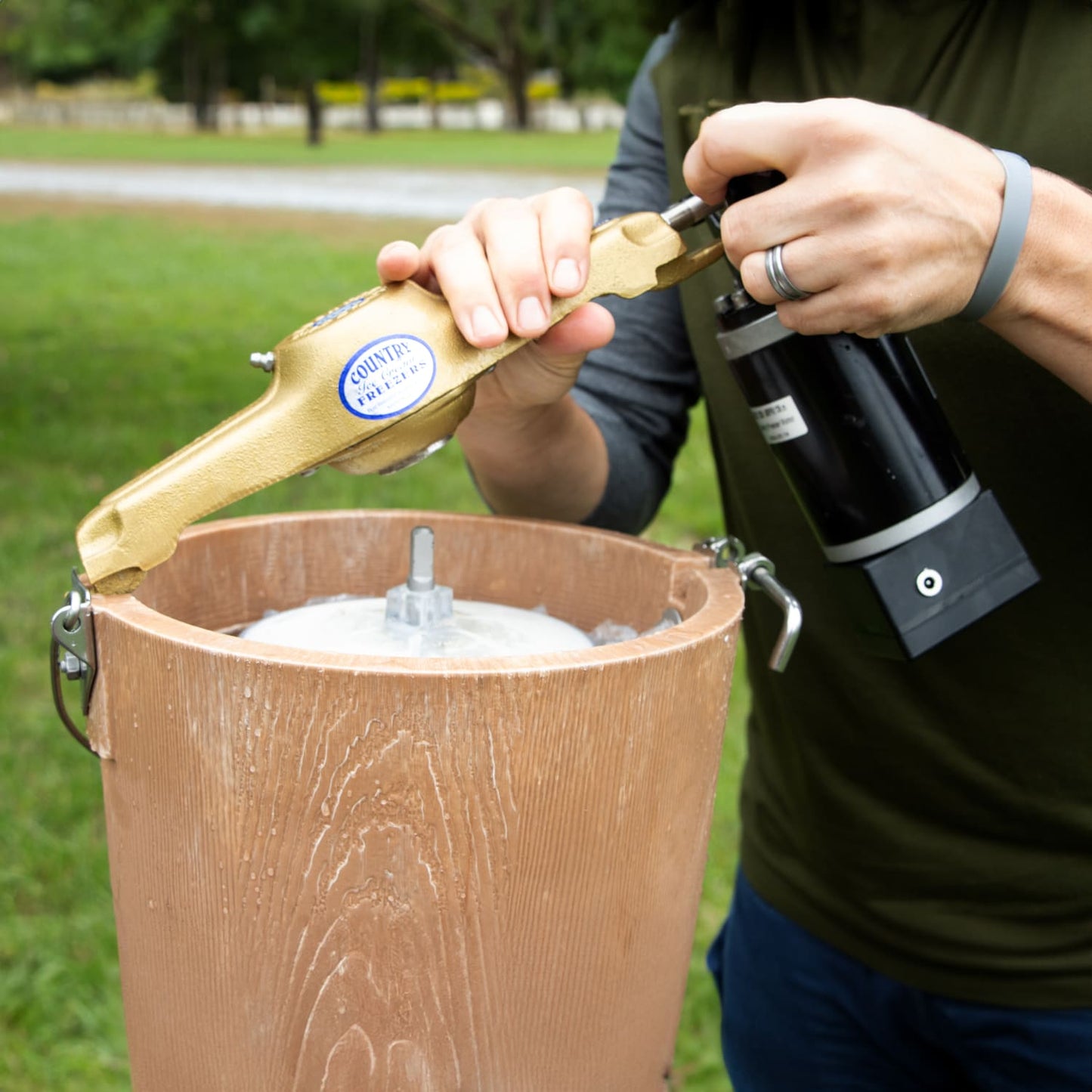 Close-up of a handcrafted Amish-made electric ice cream freezer with a poly-insulated bucket, showing a person attaching the motor drive outdoors, featured in Kitchen & Food and Specialty Equipment collections.