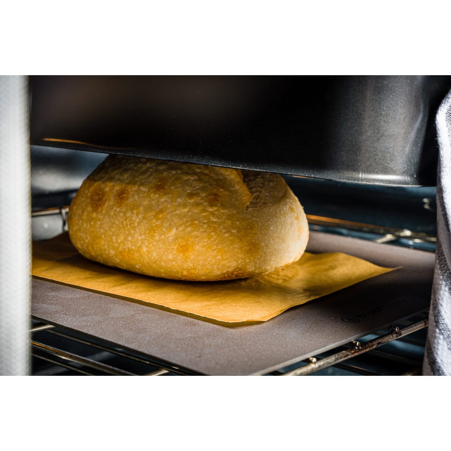 Close-up of a golden crusty batard loaf baking under a lightweight shell on a parchment-lined baking surface, showcasing cookware perfect for Kitchen & Food and Baking Supplies collections.