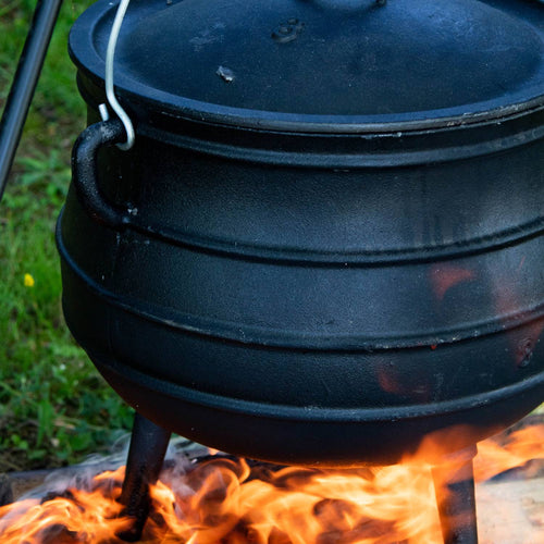 Close-up of a unique handcrafted cast iron kettle with a ribbed round body and three sturdy legs, sitting over an open flame, perfect for Farm, Garden & Tool, Camping, and Best Sellers collections.