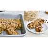 Aluminized steel baking pan holding freshly baked oat and chocolate chip bars with a few bars served on a white plate, styled in a kitchen setting with a jar of oats nearby, fitting Kitchen & Food and Baking Supplies collections.