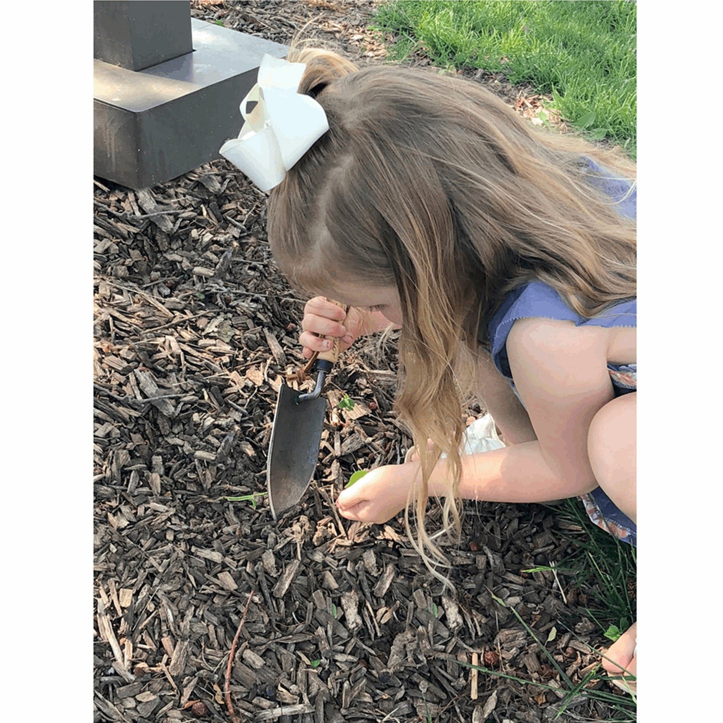 Young child using a small gardening trowel to dig in wood chip mulch near grass, illustrating a tool suited for small hands and garden care in Farm, Garden & Tool collections.