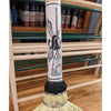 Close-up of the handle of an Amish made authentic corn straw broom with hand-sewn binding, displayed indoors on a wooden floor among cleaning tools and supplies.
