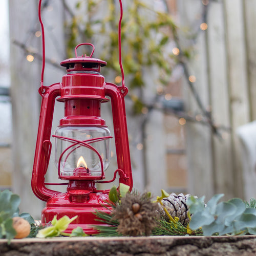 Handcrafted bright red galvanized oil lantern with thermal heat-resistant SUPRAX globe lit outdoors on rustic wooden surface surrounded by seasonal greenery, ideal for Lamps & Lighting, Camping, Emergency Supplies, and Outdoors collections.