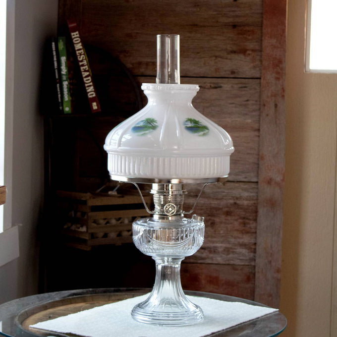 Classic oil lamp with clear glass base and white glass shade featuring painted tropical beach scenes; fits standard 10-inch shade rings, perfect for lamps and lighting collections.
