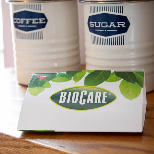 Folded BioCare card-style pantry moth trap with green leaf design, placed on wooden surface near vintage-style coffee and sugar canisters, suitable for Home & Decor and Pest Control collections.
