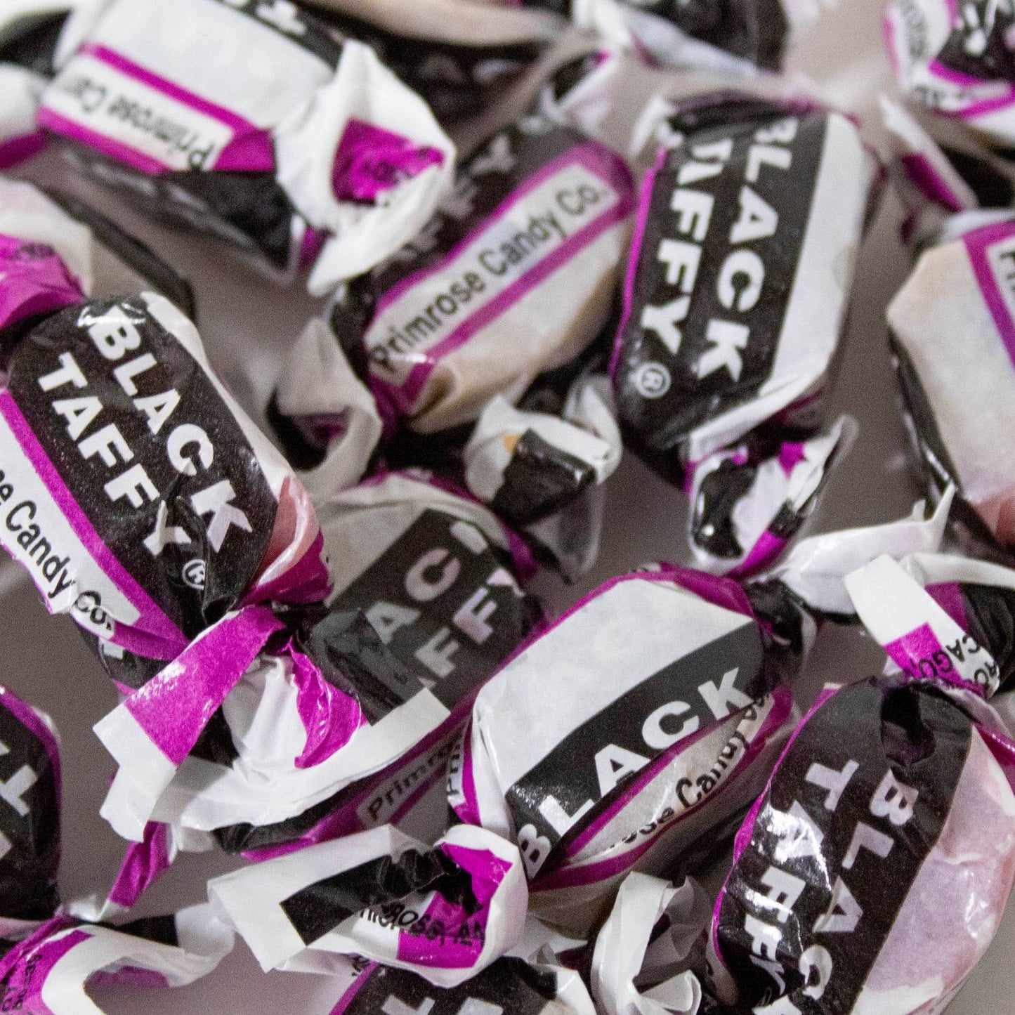 Close-up of individually wrapped black taffy candies with black, white, and purple packaging, highlighting handcrafted nostalgic sweets from Kitchen & Food, Food, Snacks and Sweets, Best Sellers, and Promo Eligible collections.