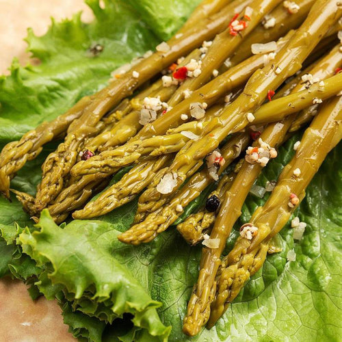 Close-up of handcrafted pickled asparagus spears seasoned with spices and placed on fresh green lettuce, highlighting a tangy, locally made pantry item from Amish Country.