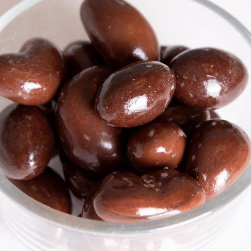 Close-up view of shiny milk chocolate coated nuts in a clear glass bowl, handcrafted in the USA, perfect for Kitchen & Food, Snacks and Sweets, Candy, USA Made, and Best Sellers collections.