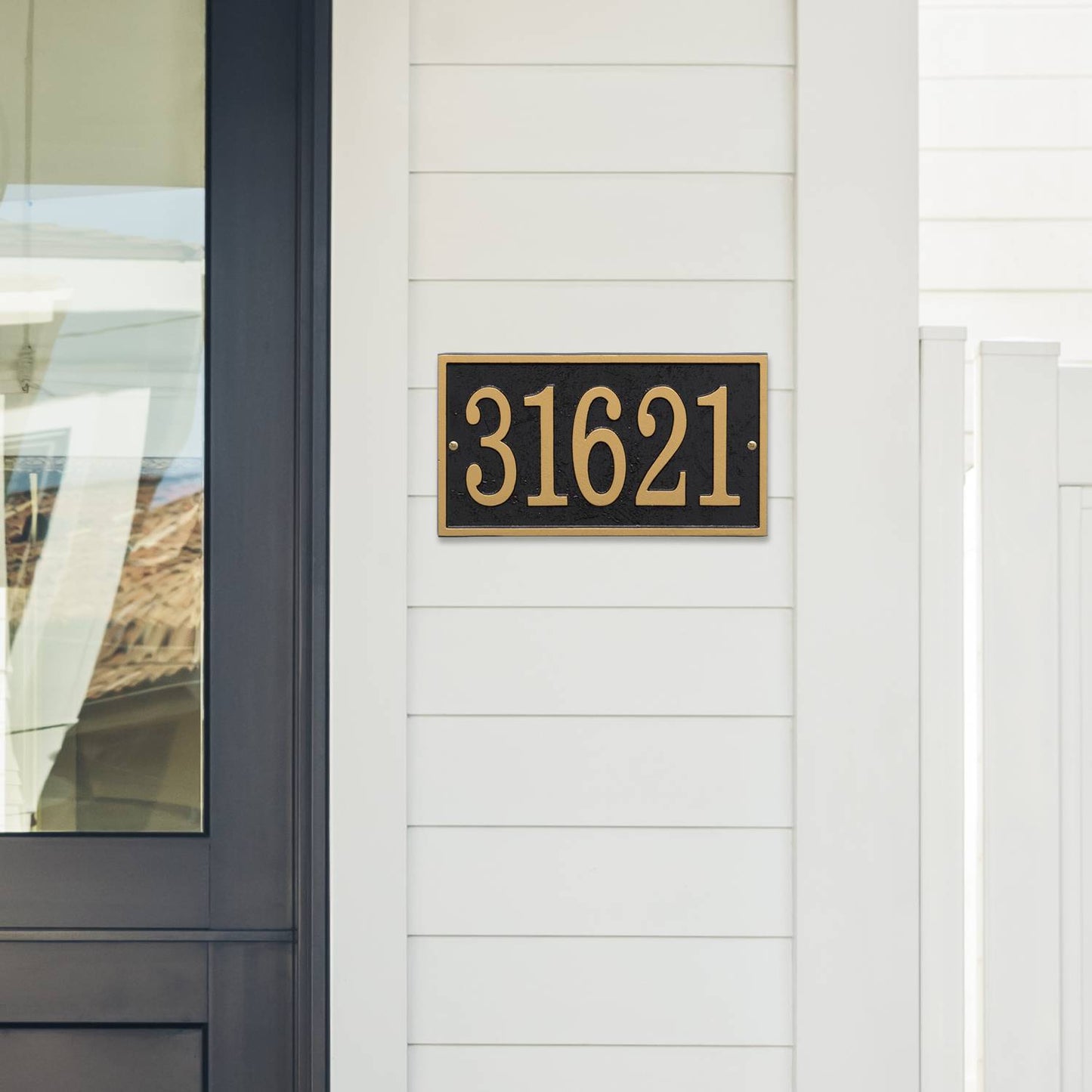 Black and gold rectangular custom address plaque with bold numbers mounted on white siding near a dark door, handcrafted in USA for Home & Decor, Household Helpers, and Mailboxes and Address Signs collections.