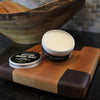 Open tin of cutting board wax conditioner with white wax and black label resting on a two-tone wooden cutting board, featured in Kitchen & Food, Food Prep, and Best Sellers collections.