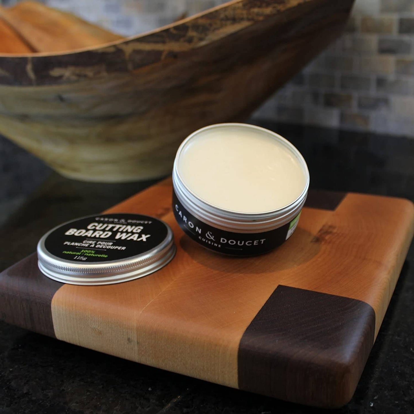 Open tin of cutting board wax conditioner with white wax and black label resting on a two-tone wooden cutting board, featured in Kitchen & Food, Food Prep, and Best Sellers collections.