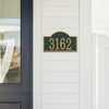 Handcrafted green and gold arched address plaque with bold numbers mounted on white siding, designed to enhance curb appeal, made in USA, ideal for Home & Decor and Mailboxes and Address Signs collections.