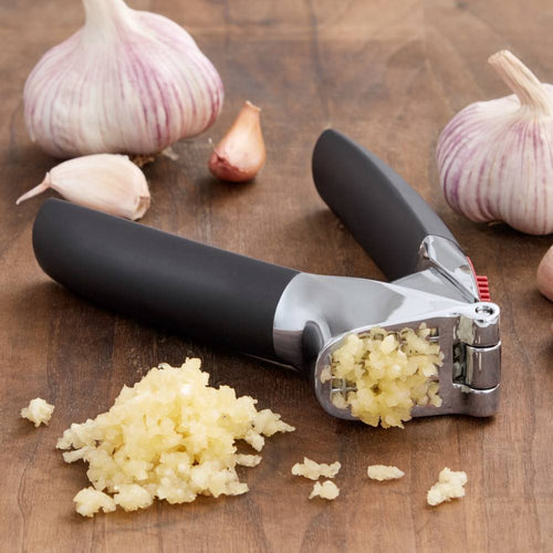 Garlic press with large stainless steel chamber and soft, non-slip black handles crushing fresh garlic cloves on a wooden surface, ideal for Kitchen & Food and Kitchen Gadgets collections.