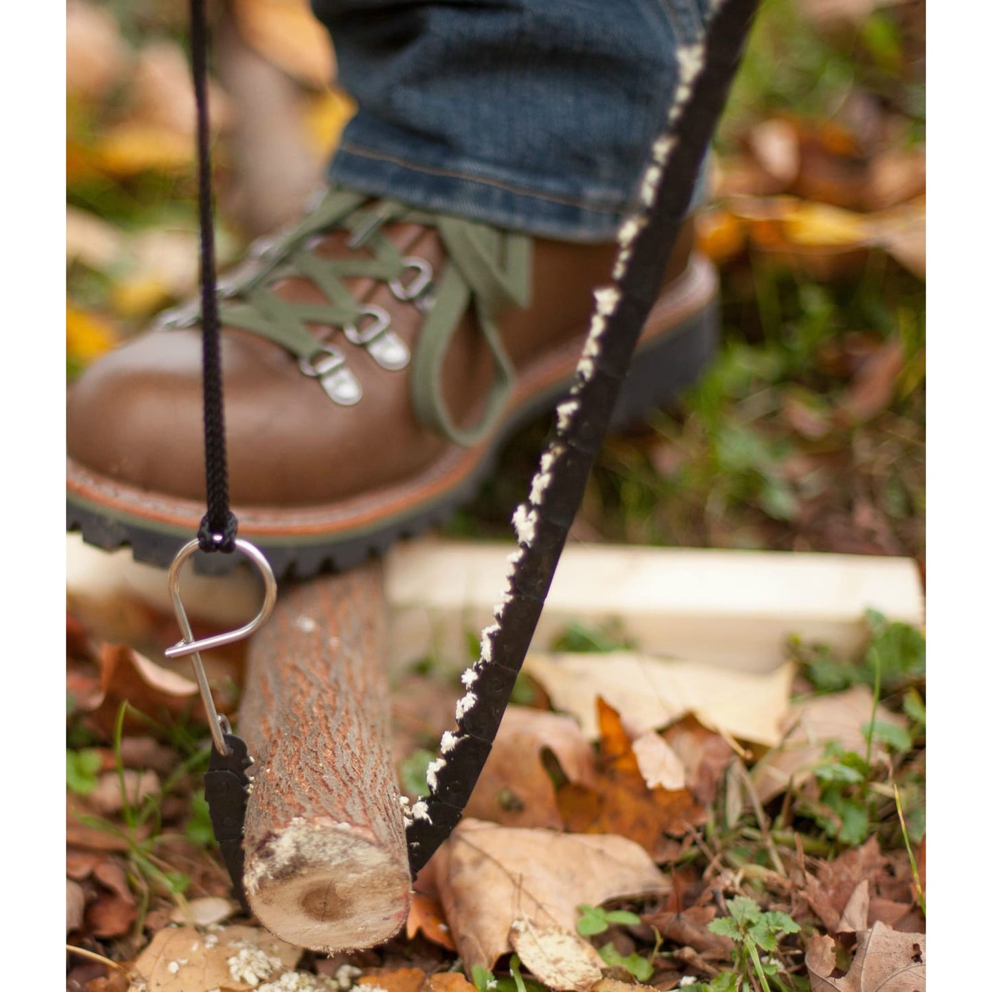 Close-up of a person using a compact handcrafted pocket chain saw to cut a small branch on the ground, showcasing its sharp teeth and sturdy handle, made in USA, ideal for Farm, Garden & Tool and Camping collections.