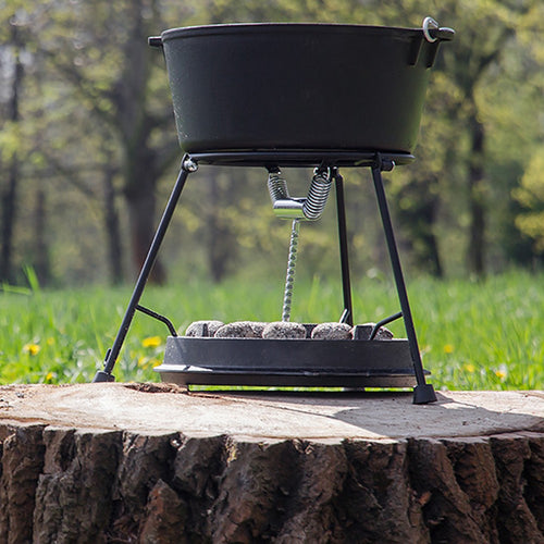 Petromax cast iron Dutch oven with flat base cooking over charcoal briquettes on a sturdy tripod stand outdoors, ideal for Kitchen & Food, Cookware, Cast Iron, Best Sellers collections.
