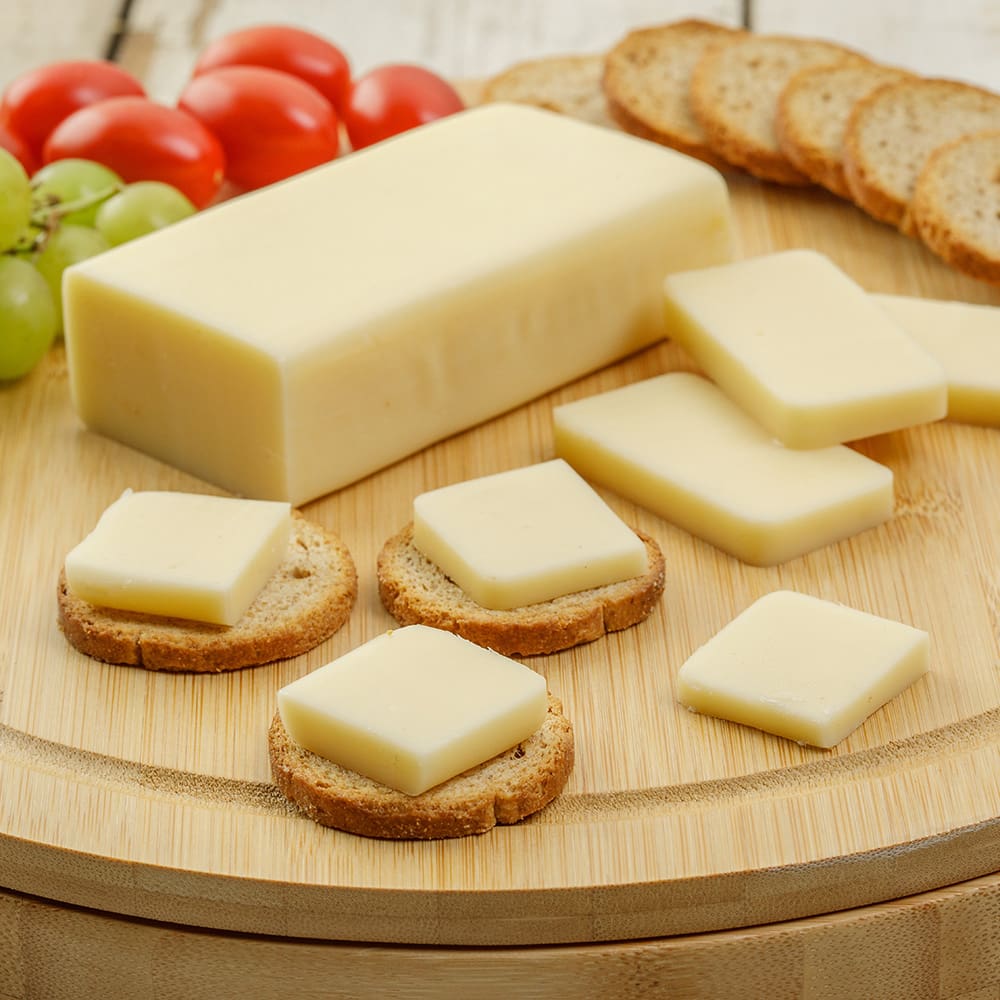 Handcrafted block of shelf-stable cheese with several square slices arranged on round crackers, accompanied by fresh grapes, cherry tomatoes, and oat crackers, perfect for Kitchen & Food, Snacks and Sweets, Pantry, USA Made, and Best Sellers collections.