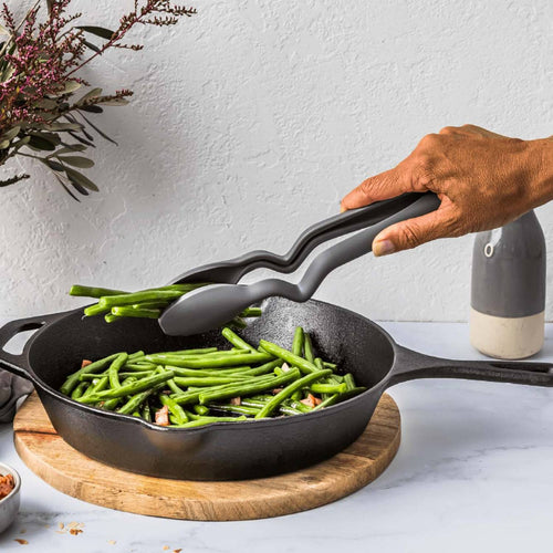 Dark gray nylon cooking tongs with a bent handle design to keep tips elevated, shown lifting green beans from a cast iron skillet, ideal for Kitchen & Food, Kitchen Gadgets, and Best Sellers collections.