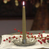 Handcrafted olive-green bayberry candle burning in a rustic pewter holder, displayed with decorative red berries on a white lace cloth, reflecting traditional holiday decor.