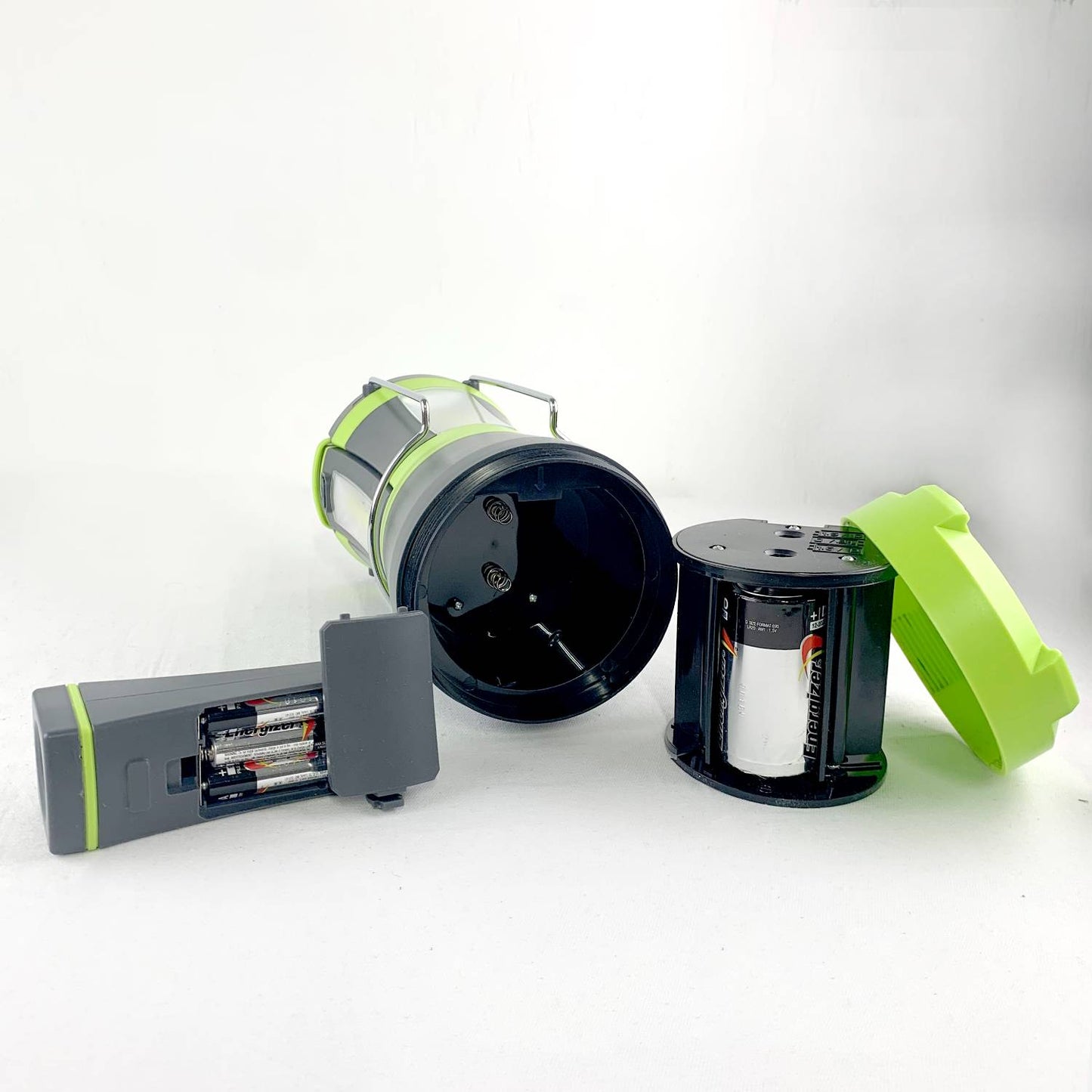 Disassembled green and black LED lantern with battery compartments exposed, showcasing components designed for versatile lighting in camping, emergency supplies, and outdoor use.