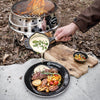 Hand pouring creamy sauce from a small cast iron pan over grilled steak and vegetables on a black plate outdoors, next to a fire pit, suitable for Farm, Garden & Tool, Kitchen & Food, Camping, Cookware, Cast Iron, Best Sellers, and Promo Eligible collections.