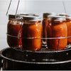 Glass jars filled with homemade preserves in a metal canning rack, being processed in a large black enamelware pot, featured in Kitchen & Food and Food Preservation collections.