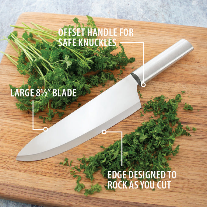Chef's knife with an 8-1/2-inch blade featuring an offset handle to protect knuckles, designed for rocking cuts while dicing herbs on a wooden cutting board, made in USA.