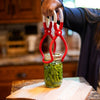 Hand lifting two glass jars filled with green beans using a red and white one-handed jar lifter in a warm kitchen setting, part of Kitchen & Food and Food Preservation collections.