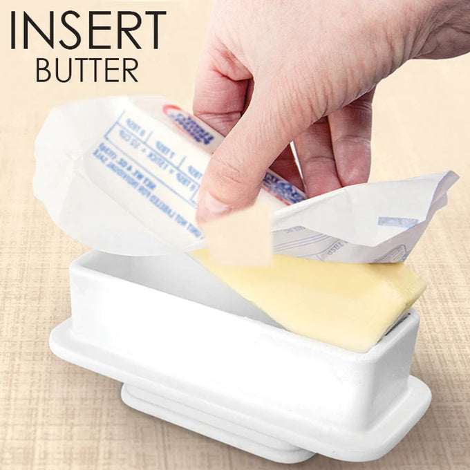 Hand placing a full quarter stick of butter, partially wrapped, into a simple white ceramic butter keeper base, part of Kitchen & Food and Specialty Equipment collections.
