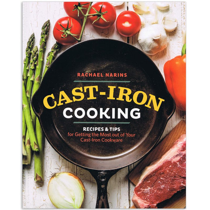 Paperback cookbook titled Cast-Iron Cooking by Rachael Narins, featuring a cast iron skillet surrounded by fresh vegetables and a raw steak, highlighting kitchen and cookware themes.