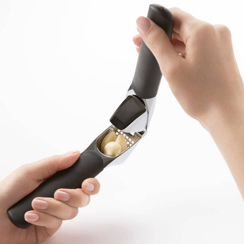 Hands using a garlic press with soft, non-slip black handles and a large stainless steel chamber crushing multiple garlic cloves, designed for ease in Kitchen & Food, Kitchen Gadgets, and Cooking and Baking Helpers collections.