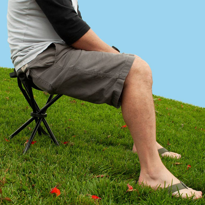 Person seated on a compact four-legged folding camping stool with black metal frame on grass, designed for lightweight outdoor use in Farm, Garden & Tool, Camping, Best Sellers, Promo Eligible, and Sale collections.