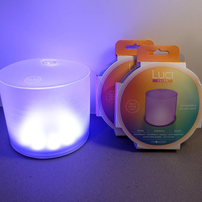 Soft glowing inflatable solar LED light in soothing blue hue next to two compact, color-changing Luci Color Essence Solar Light packages, ideal for camping and outdoor lighting.