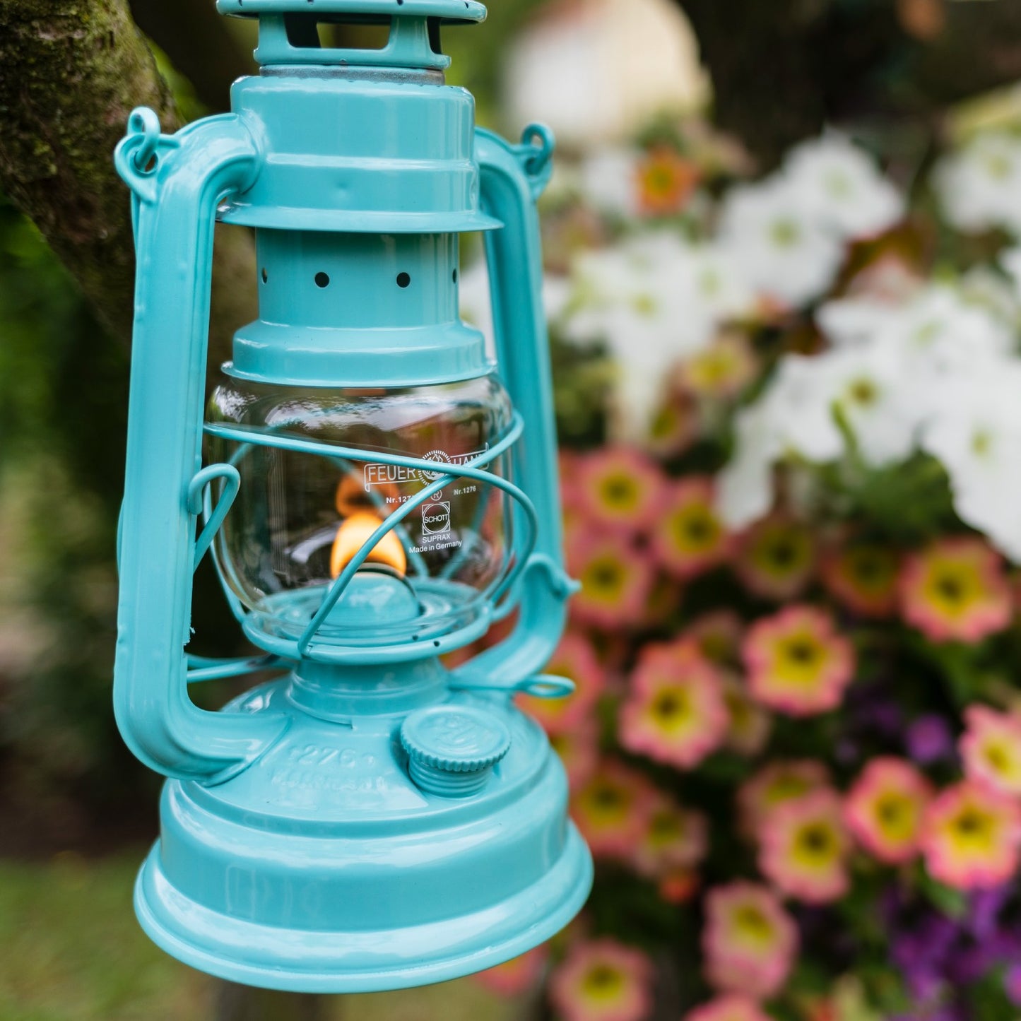 Handcrafted turquoise galvanized oil lantern with heat-resistant SUPRAX globe softly glowing outdoors near blooming flowers, ideal for Camping, Lamps & Lighting, and Emergency Supplies collections.
