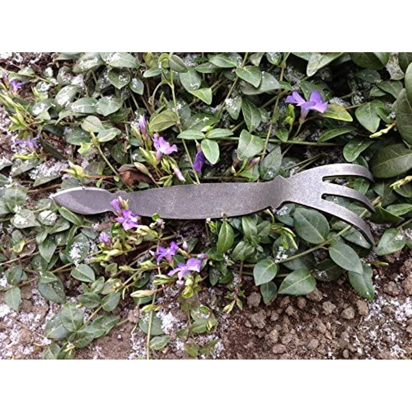 Handcrafted all-steel cultivator with a three-pronged fork and cobra-shaped head resting on green foliage with purple flowers, ideal for Farm, Garden & Tool and Digging and Cultivating collections.