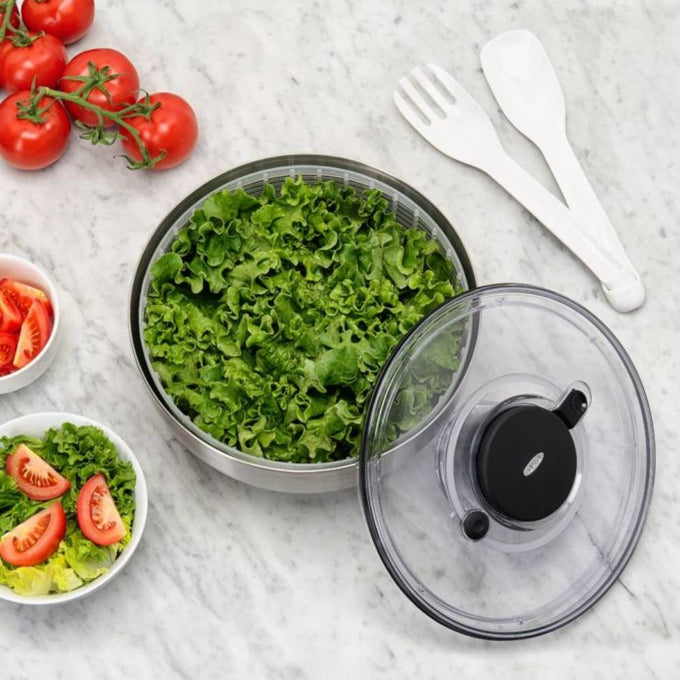 Clear-lid salad spinner with fresh green lettuce inside and plastic serving utensils on marble countertop, accompanied by fresh tomatoes and salad bowls, ideal for Kitchen & Food and Kitchen Gadgets collections.