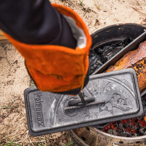 Gloved hand using a curved metal lifter to safely remove a hot cast iron Dutch oven lid over an outdoor campfire, featured in Farm, Garden & Tool, Camping, Best Sellers, and Promo Eligible collections.