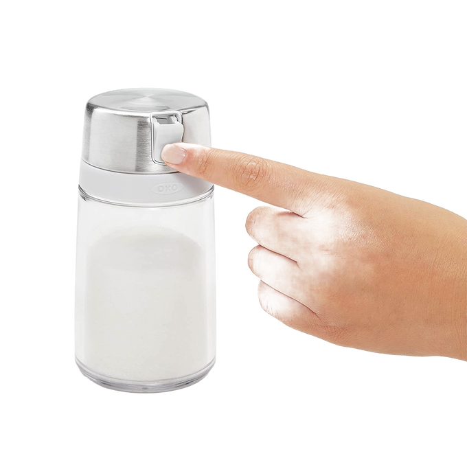 Hand pressing the stainless steel flip-top lid of a clear glass sugar dispenser designed to keep sugar dry and clump-free, perfect for Kitchen & Food, Kitchen Gadgets, and Storage collections.