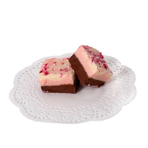 Two handcrafted peppermint-topped fudge pieces with layered creamy chocolate and vanilla flavors, presented on a white lace paper doily, part of USA made Snacks and Sweets collections.