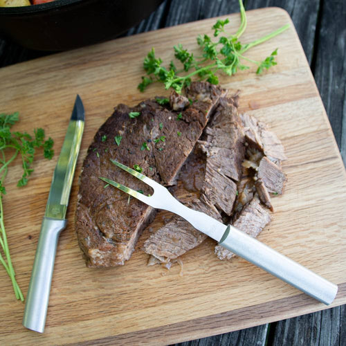 Handcrafted stainless steel carving fork with long sturdy tines resting on sliced roast beef with fresh herbs on a wooden cutting board, ideal for Kitchen & Food, Storage and Serving, USA Made, Best Sellers, and Promo Eligible collections.
